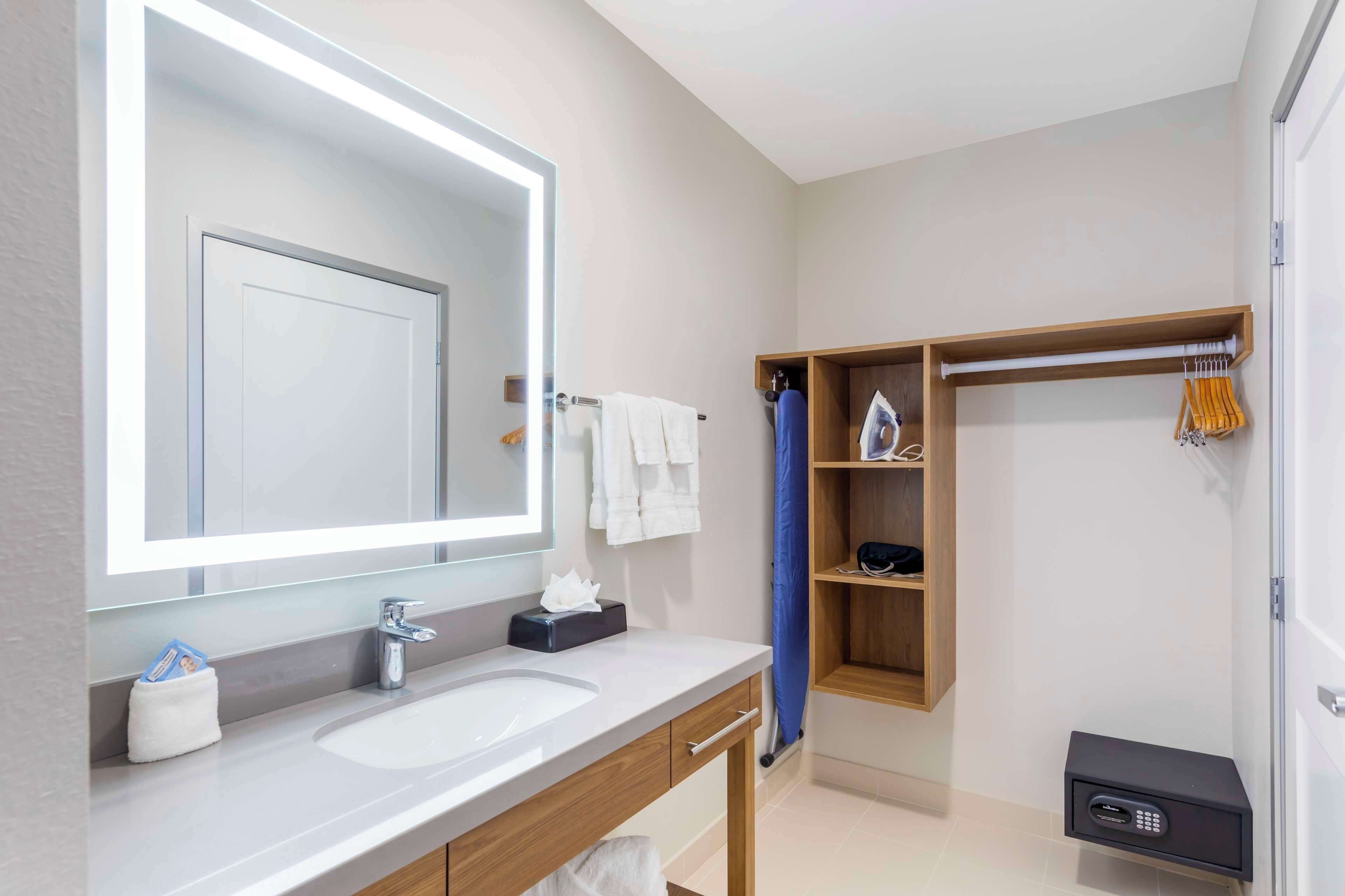 A modern bathroom with a large mirror, a sink, a towel rack, and a built-in shower area.
