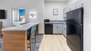A modern kitchen with a black refrigerator, white cabinets, a wooden dining table, and a blue patterned rug. - Executive Residency by Best Western Victorville (Victorville)