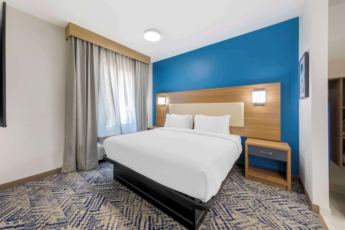 A hotel room with a large bed, a wooden headboard, a nightstand, and a blue accent wall.