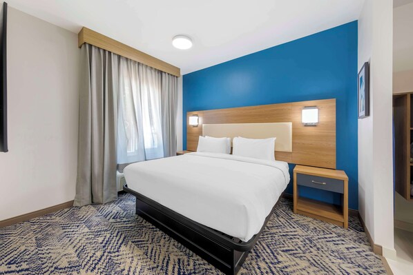 Habitación de hotel con una cama grande, cabecera de madera, mesita de noche y una pared de acento azul.