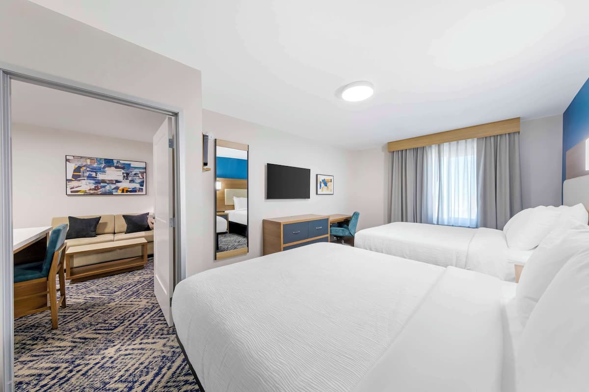 A hotel room with two beds, a desk, a chair, a sofa, a TV, and a window with curtains.