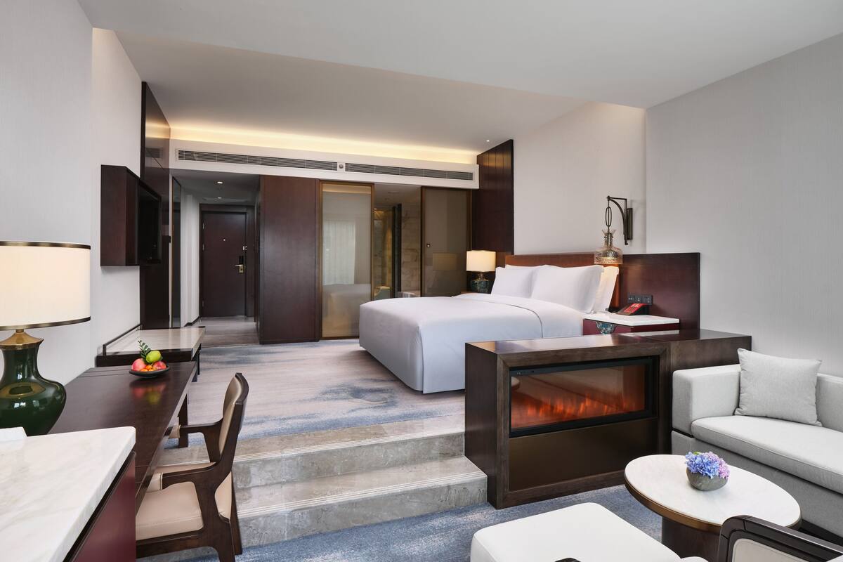 Une chambre d’hôtel comprenant un lit, un bureau, une chaise, un canapé et une petite table sur laquelle se trouve un vase.