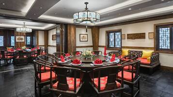 A traditional-style dining room with a round table, wooden chairs, and red cushions.