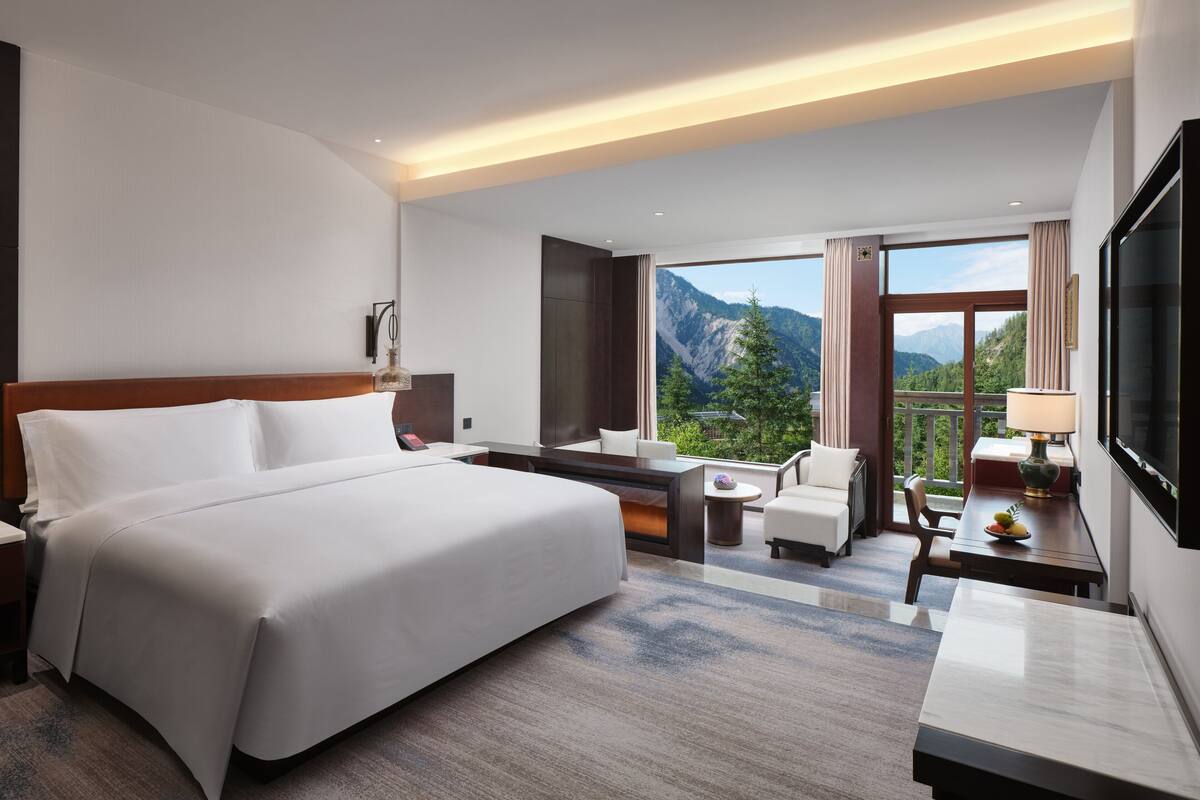 Une chambre d’hôtel avec un grand lit, un bureau, une chaise, une télévision et une vue sur les montagnes.