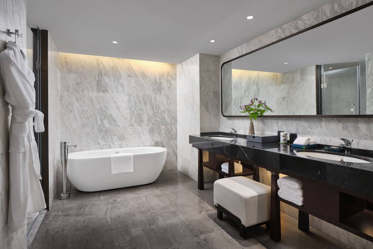 Une salle de bain moderne avec une baignoire sur pieds, un grand miroir et un meuble-lavabo doté d’un plan de travail en marbre.
