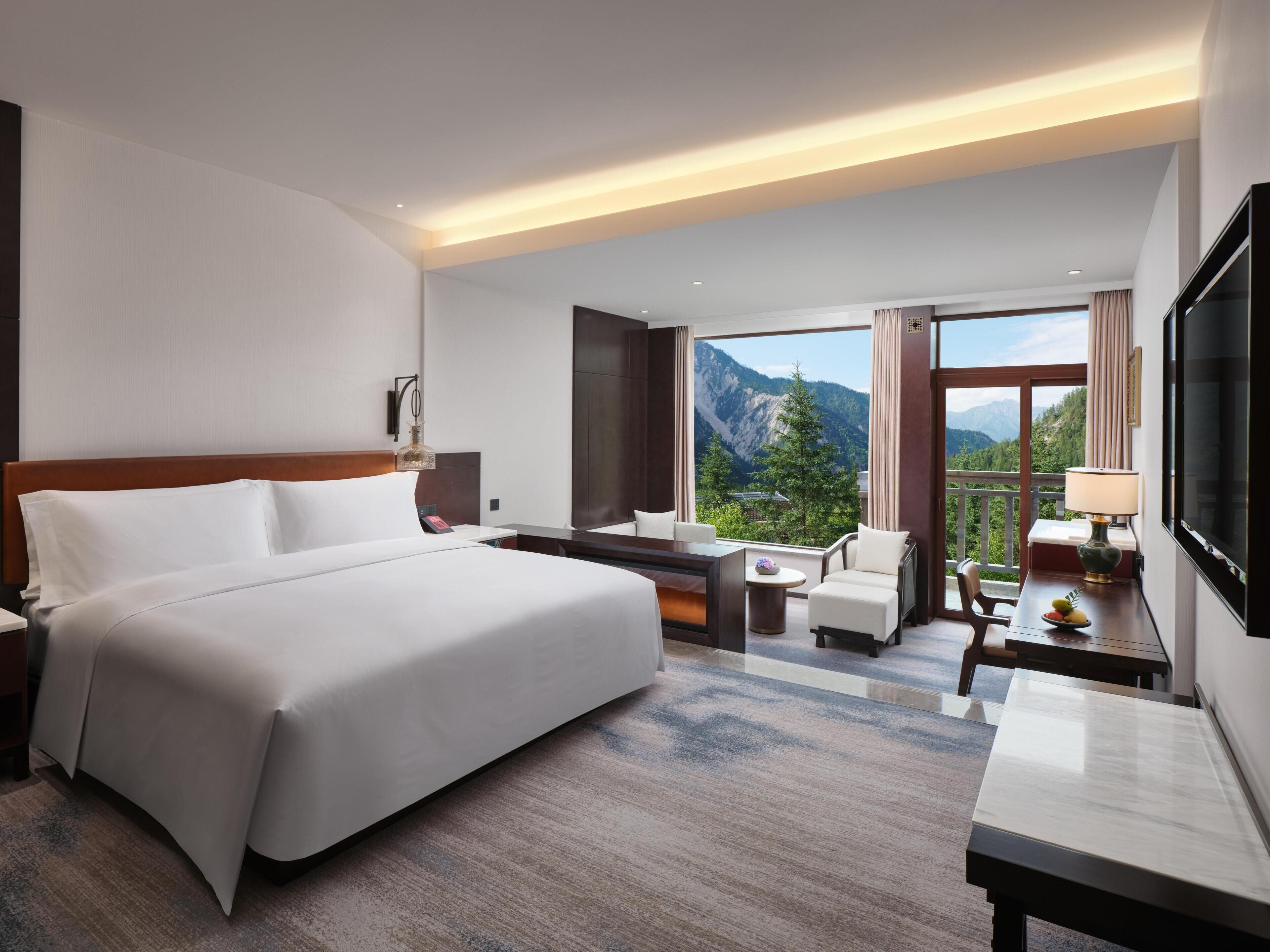 Camera d'albergo con un letto grande, una scrivania, una sedia e una televisione. C'è una finestra con vista sulle montagne.