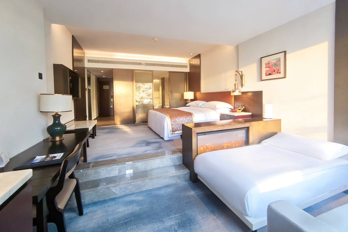 Une chambre d’hôtel avec un lit, un bureau, une chaise, une lampe et une salle de bain visible à travers une porte ouverte.