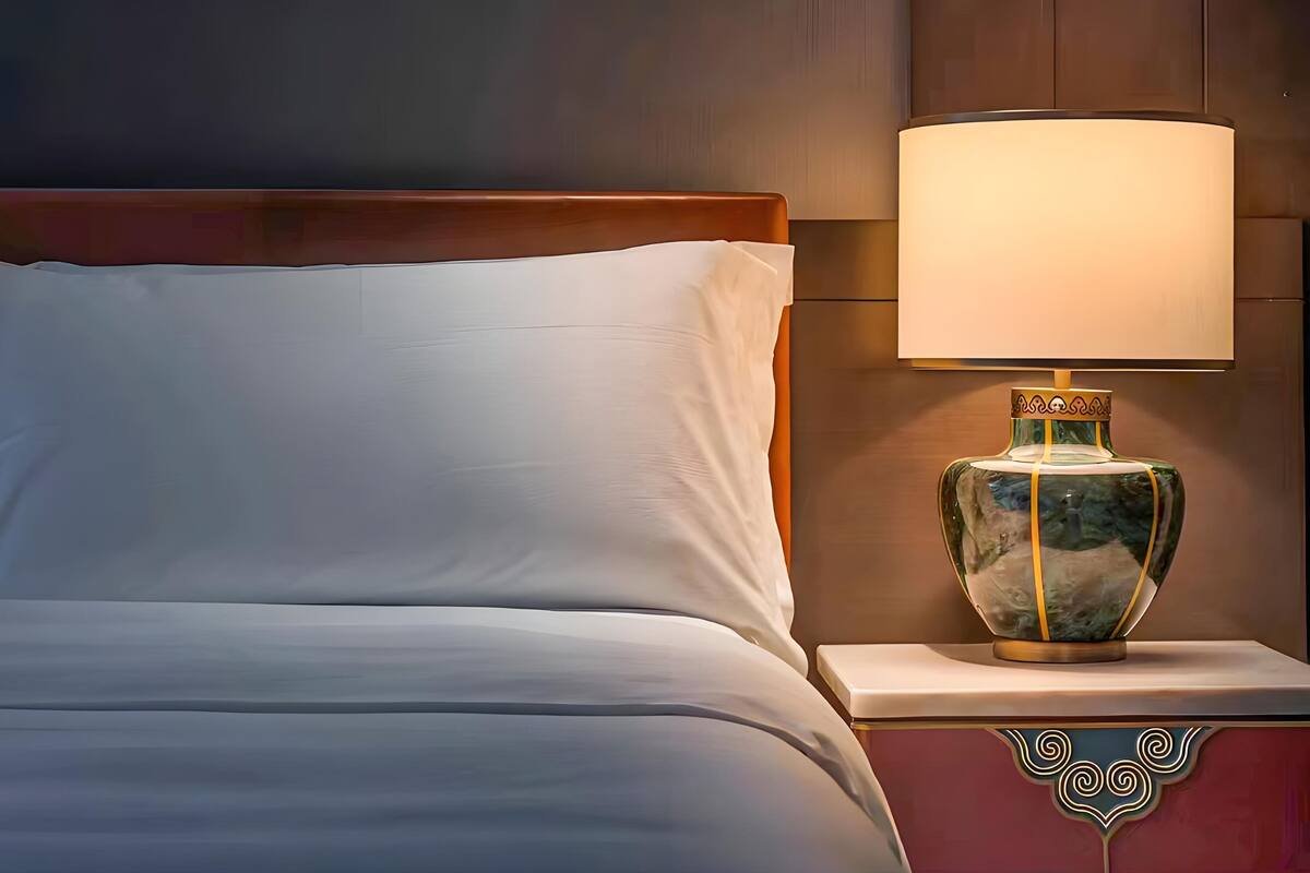 Un lit bien fait, avec du linge de lit blanc, une lampe décorative dotée d’un pied rappelant le marbre et une tête de lit en bois.