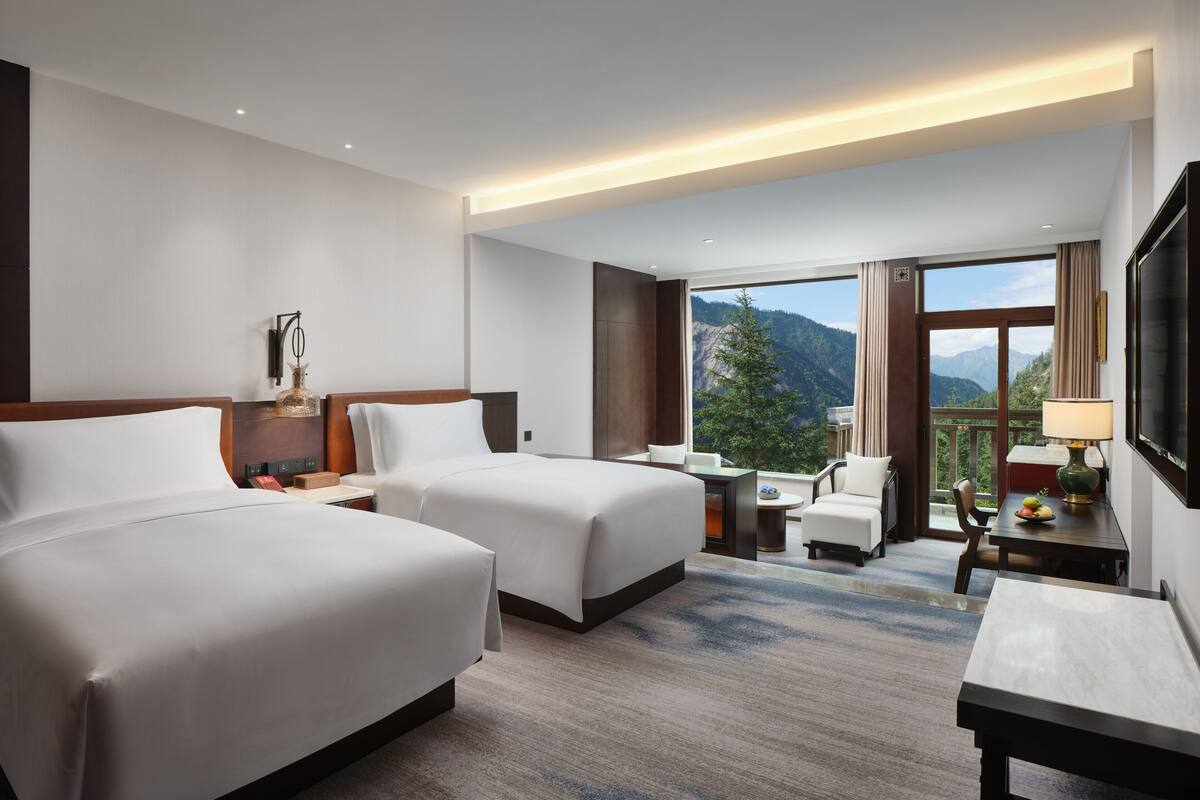 Une chambre d’hôtel avec deux lits, un bureau, une chaise et une vue sur les montagnes.