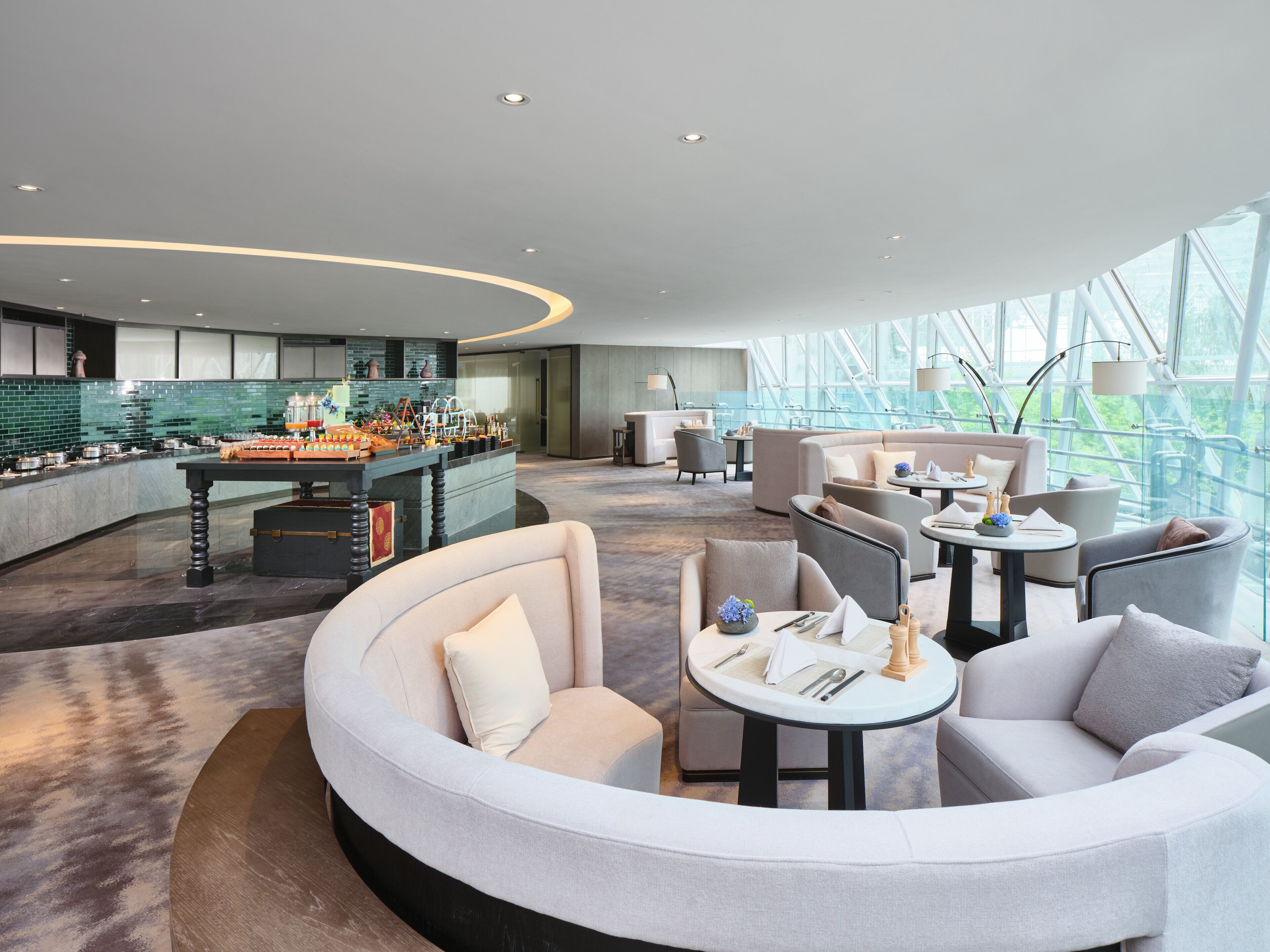 A modern hotel lobby with a curved seating area, a kitchen bar, and large windows offering a view of the outdoors.