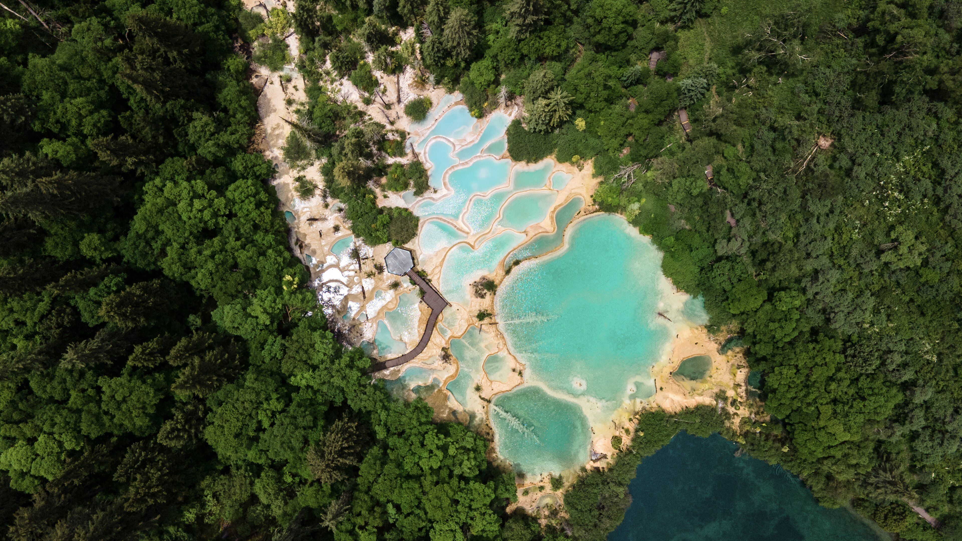 An aerial view of a natural landscape with turquoise pools surrounded by dense forest.