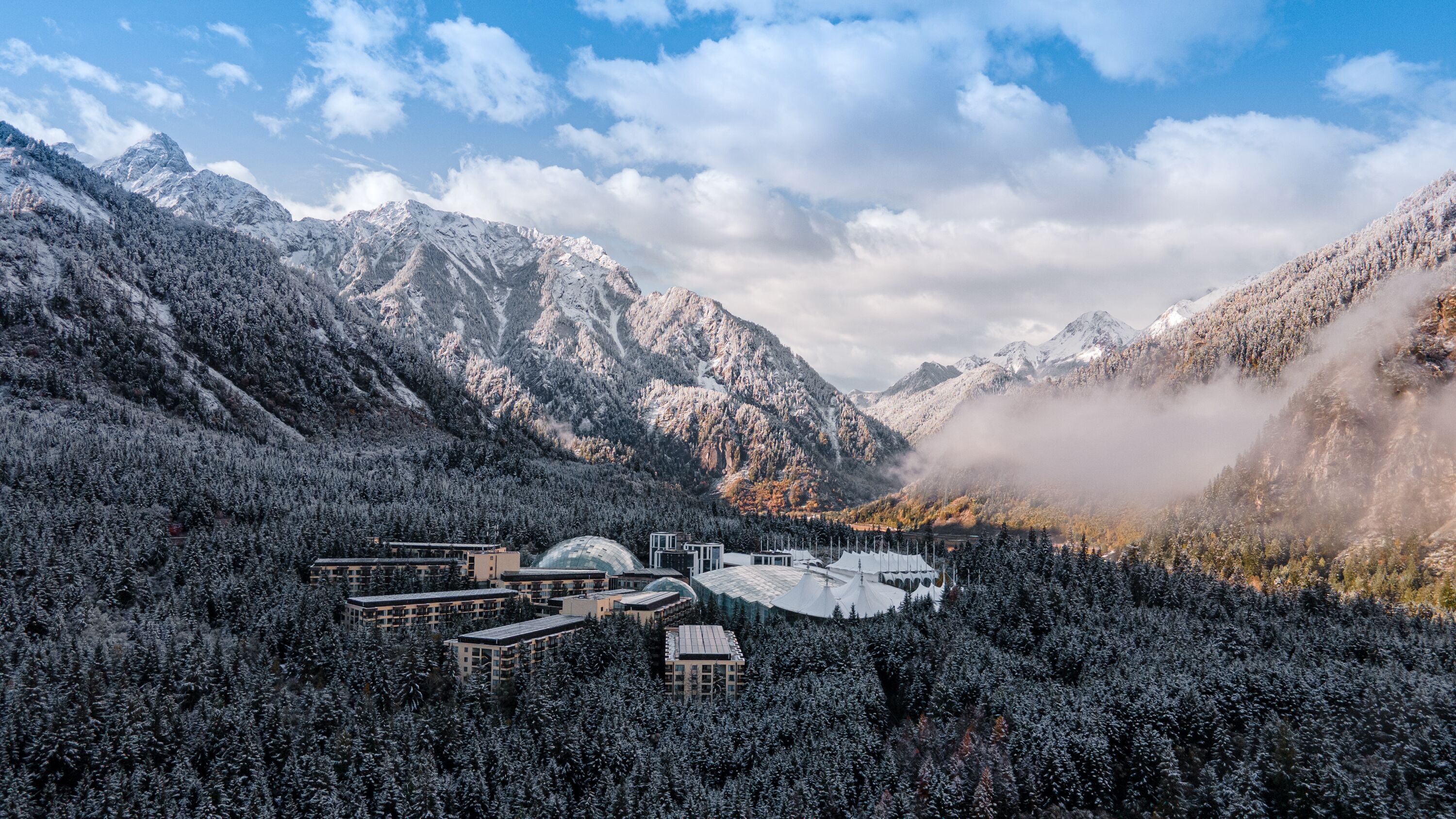 A resort with multiple buildings amidst snow-covered mountains and trees.