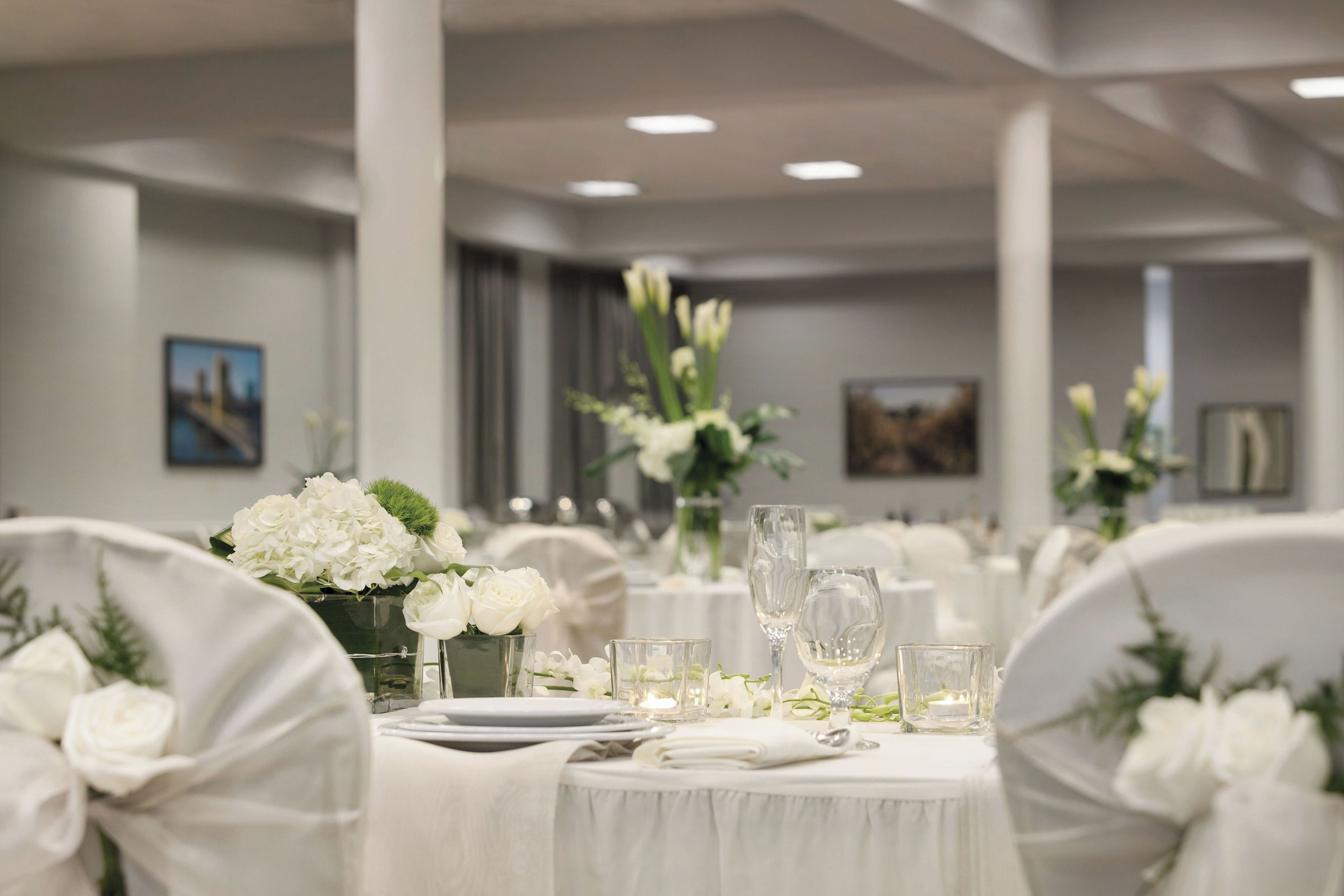 Une salle de banquet avec des tables rondes dressées pour le repas, des nappes blanches et des centres de table floraux.