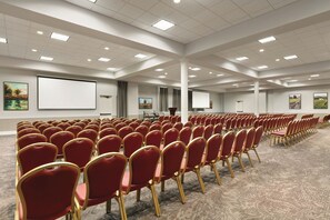 A conference room with rows of red chairs, a large screen, and a carpeted floor. - Four Points by Sheraton Sacramento International Airport (Sacramento)