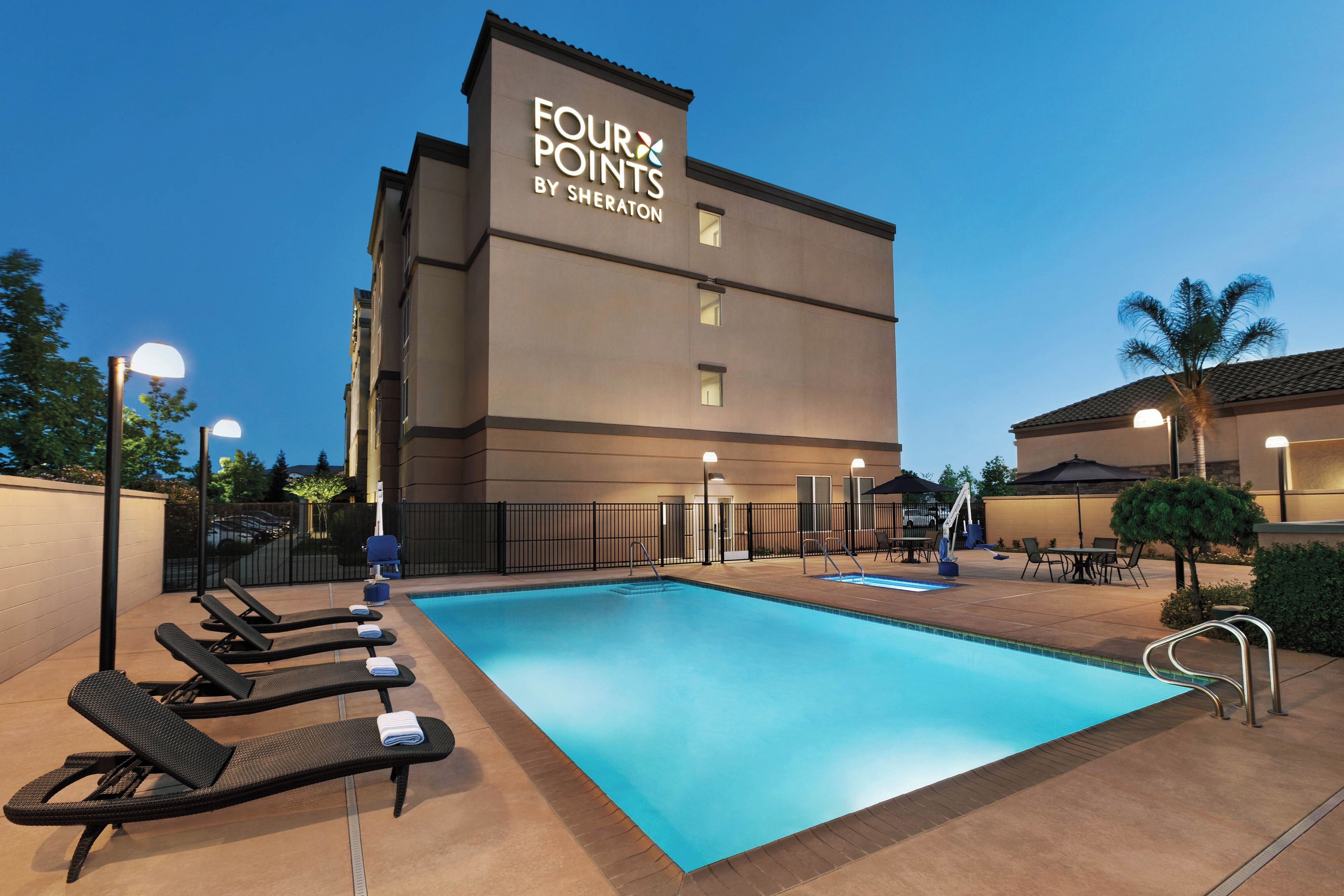 Een hotel genaamd 'Four Points by Sheraton' met een zwembad, ligstoelen en terras.