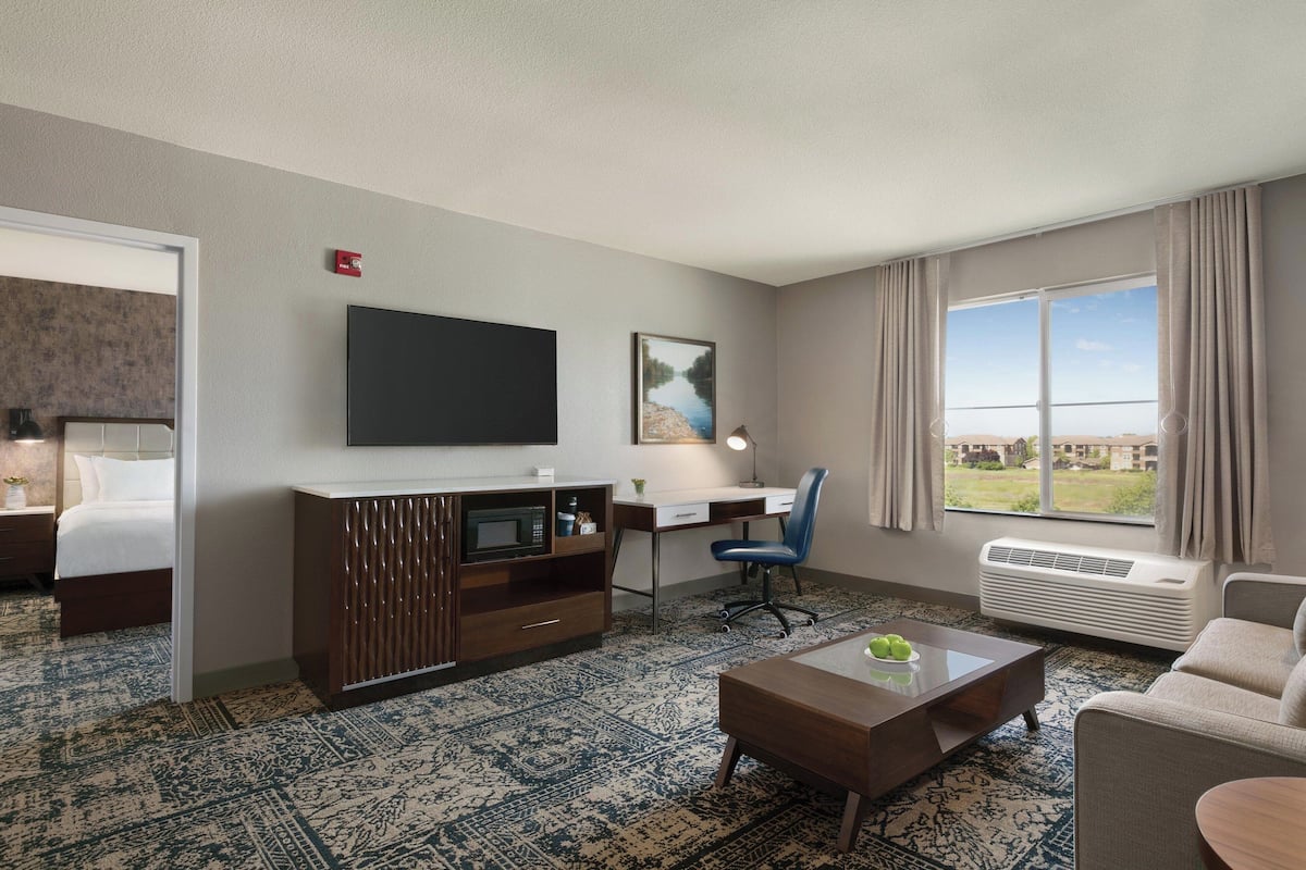 A hotel room with a bed, a desk with a computer, a TV, a coffee table, and a view of the outdoors.