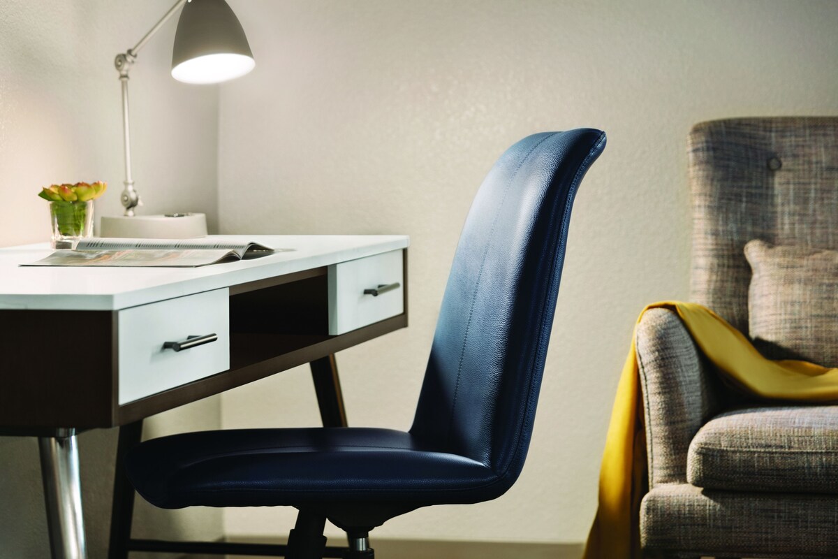 A modern office chair with a high backrest and a desk with drawers and a lamp.
