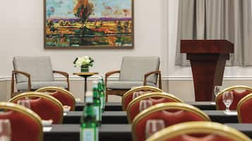 A conference room with two chairs facing a table, a podium, and a painting on the wall.