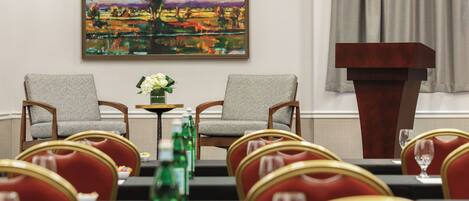 A conference room with two chairs facing a table, a podium, and a painting on the wall.