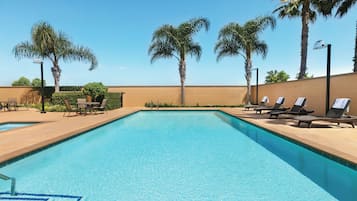 Una piscina al aire libre, sombrillas, sillones reclinables de piscina