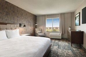 Une chambre d’hôtel avec un grand lit, une chaise, une commode, une fenêtre donnant sur un beau paysage et un tapis à motifs.