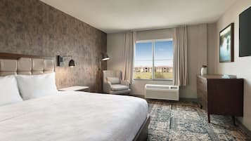 Une chambre d’hôtel avec un grand lit, une chaise, un bureau, un radiateur et une fenêtre donnant sur des immeubles.