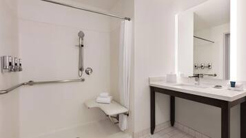 A modern bathroom with a walk-in shower, grab bars, a toilet with a towel, and a sink with a mirror.