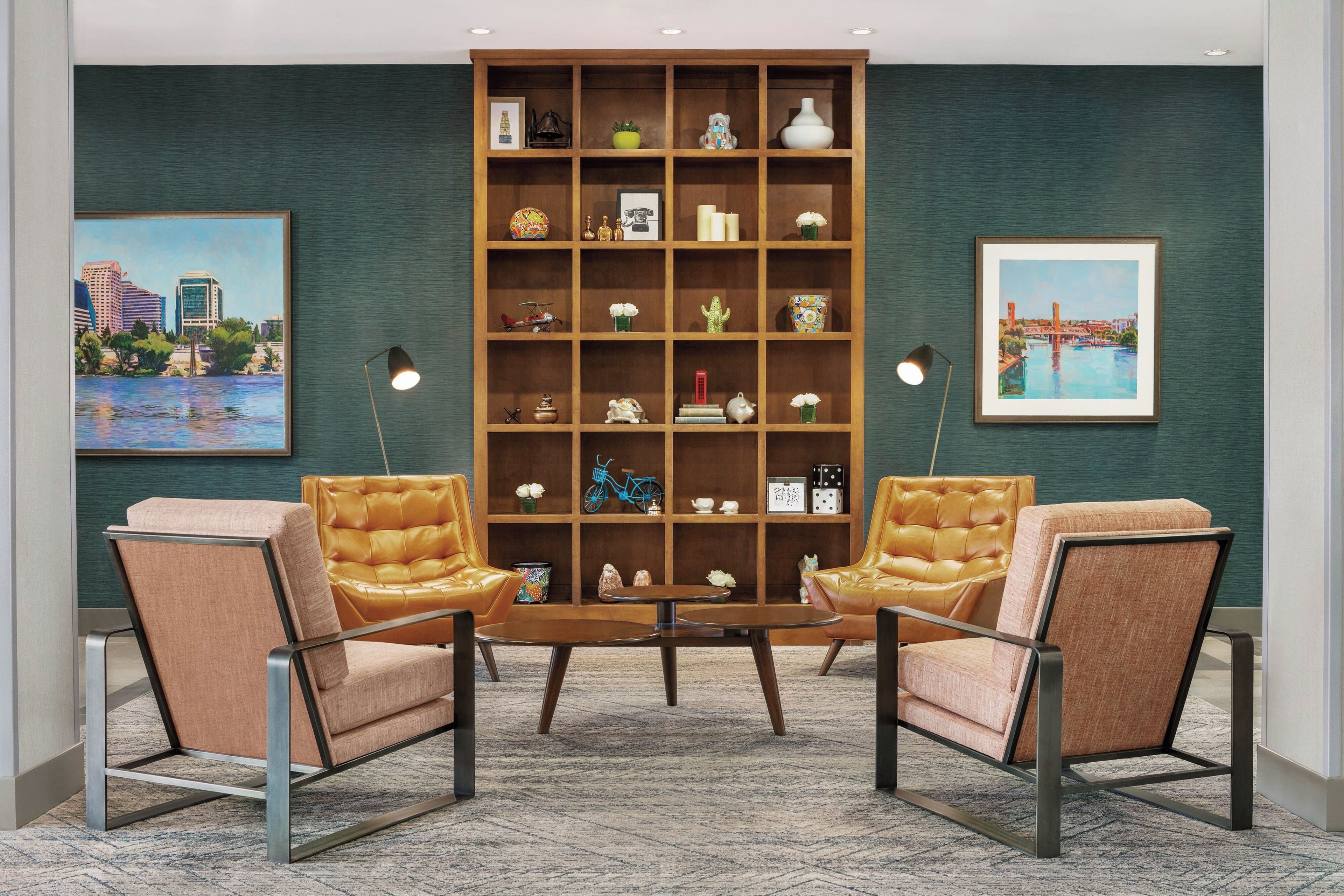 A room with a large wooden bookshelf, two leather armchairs, a coffee table, and two framed paintings on the wall.