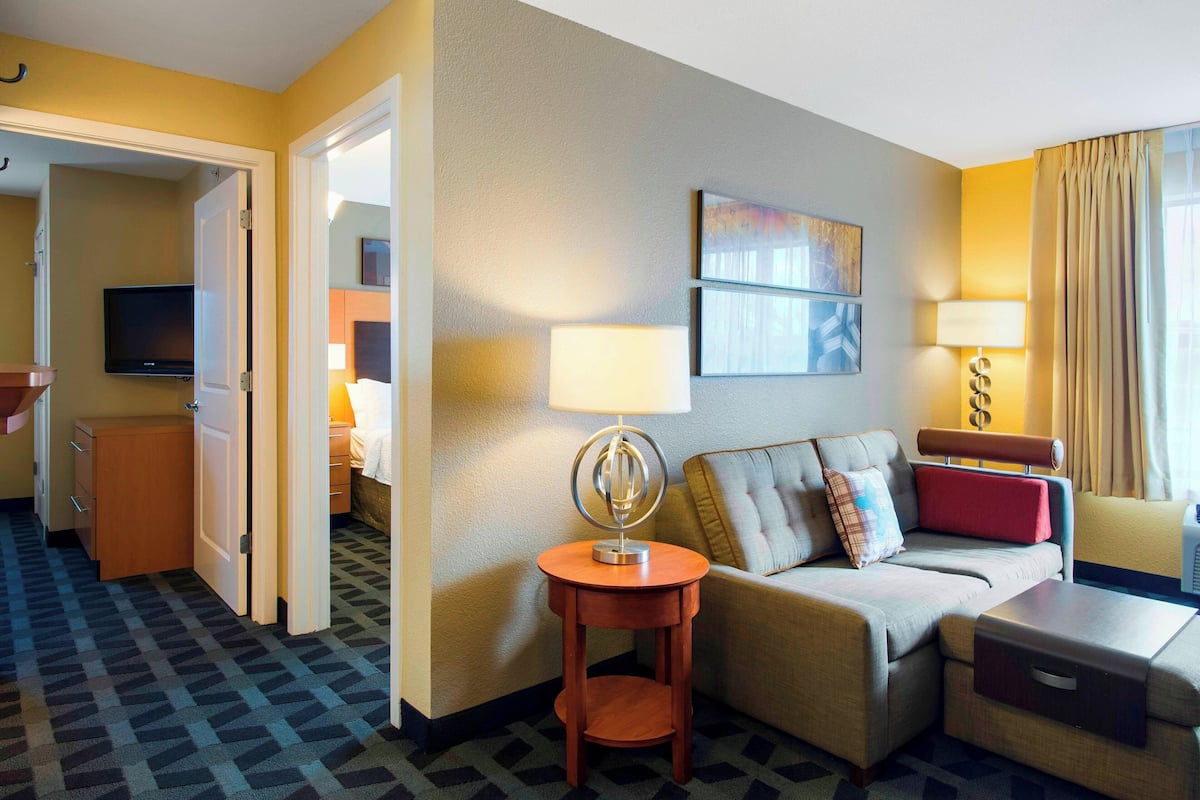 A hotel room with a sofa, a small table, a TV, and a lamp.