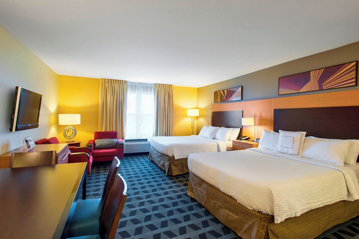 A hotel room with two beds, a desk, a chair, and a TV.