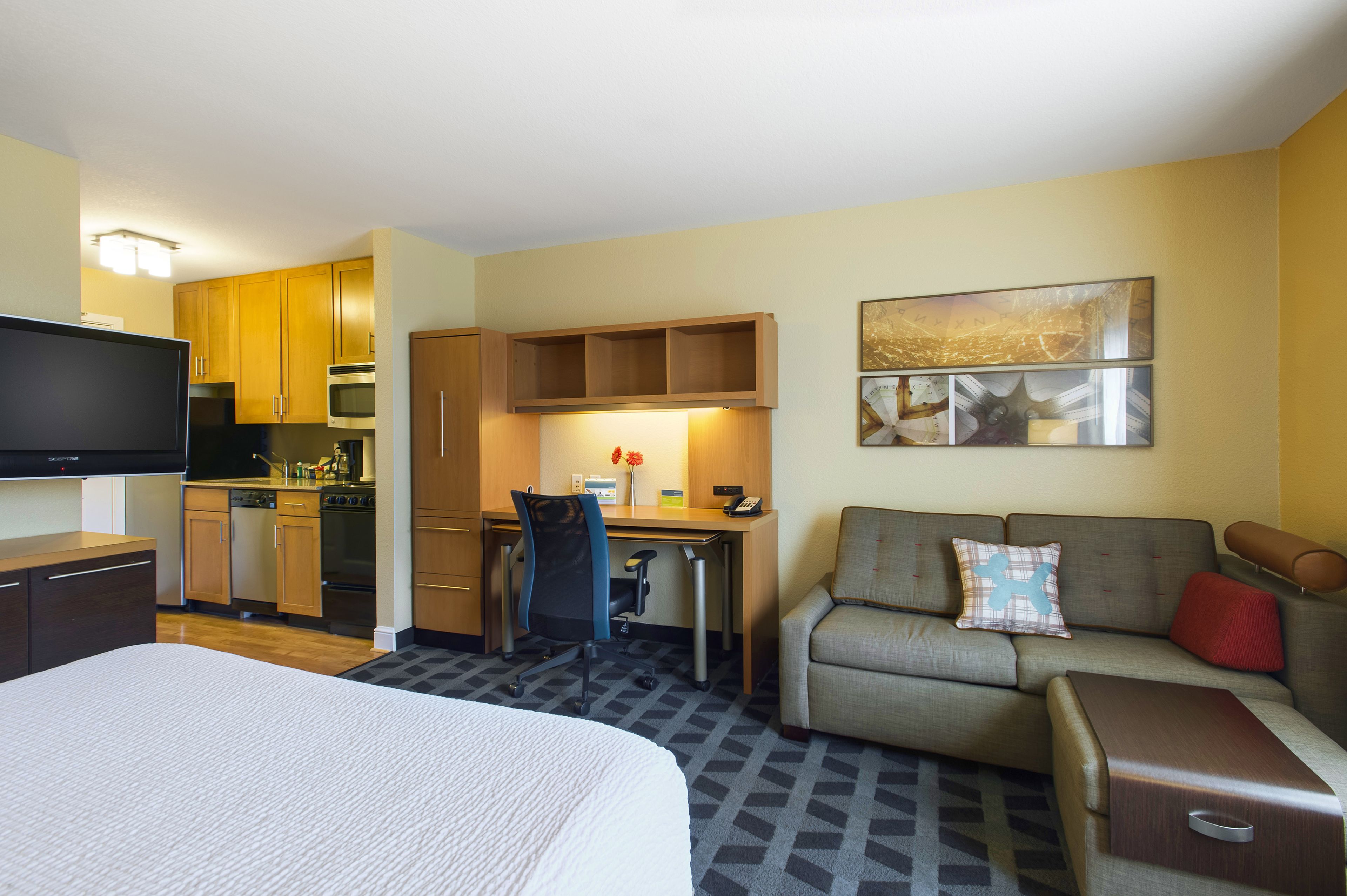 Habitación de hotel con cama, escritorio, sofá, televisor y kitchenette.