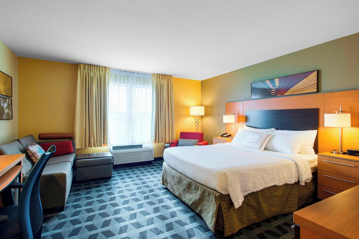 A hotel room with a bed, a sofa, a desk, and a window with curtains.