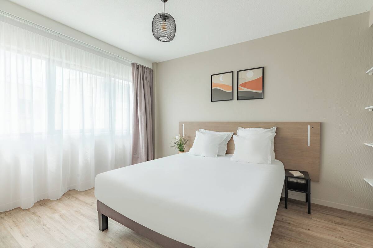 Una habitación de hotel moderna con una cama grande, una mesita de noche y una pequeña planta.