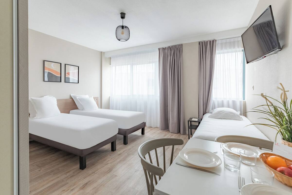 Habitación de hotel con dos camas, una mesa de comedor con platos y vasos, un televisor y una planta.
