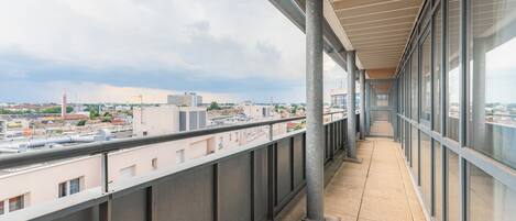 Un largo pasillo con barandilla metálica, ventanas amplias y vistas a la ciudad.