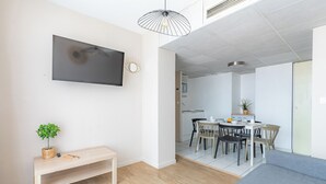 Een moderne woonkamer met een flatscreen televisie, een houten bankje, een potplant en een grijze bank.