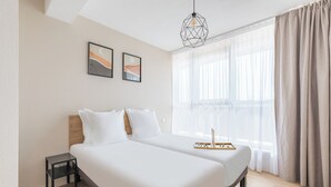 Een moderne hotelkamer met een groot bed, een nachtkastje en een raam met dunne gordijnen.