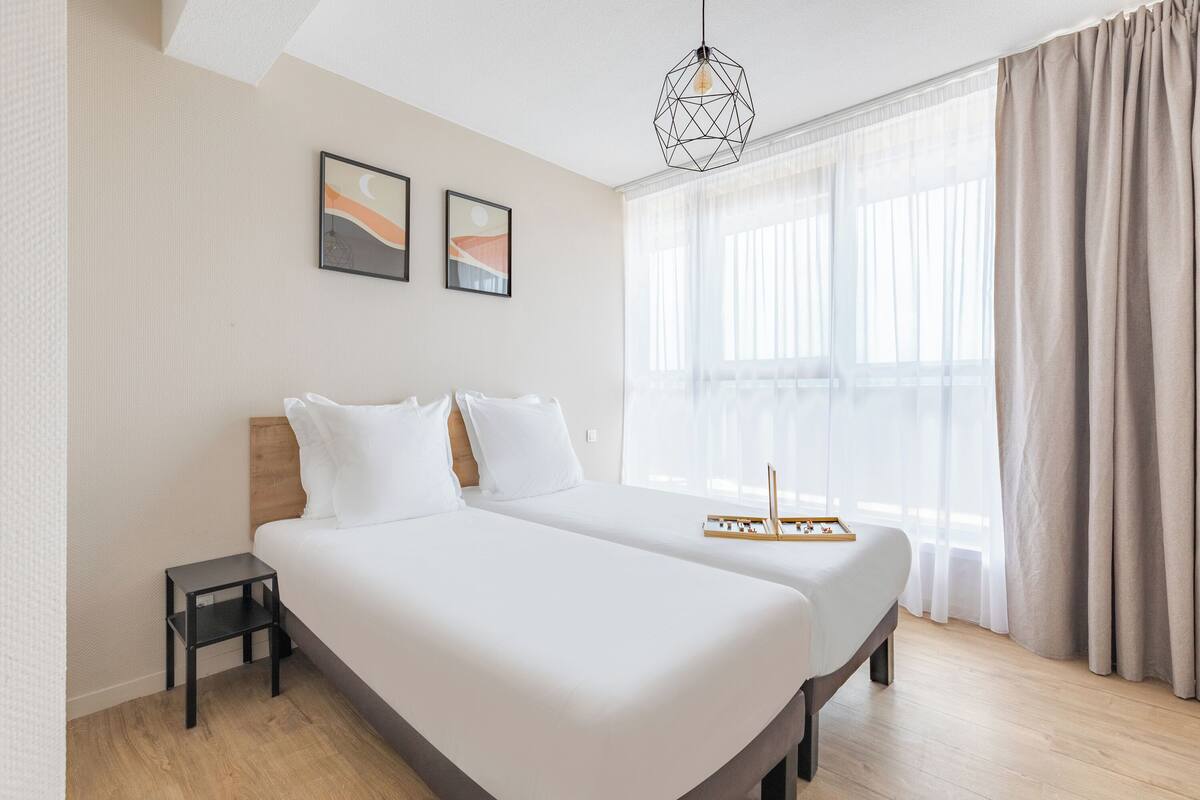 Una habitación de hotel moderna con una cama grande, una mesita de noche y una ventana con cortinas traslúcidas.
