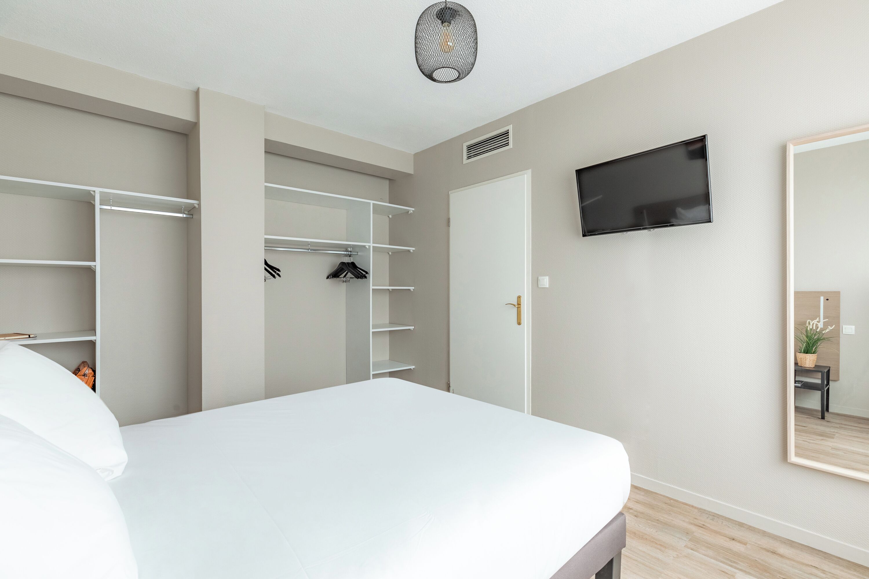 Une chambre à coucher avec un lit, une armoire, une télévision et un miroir.