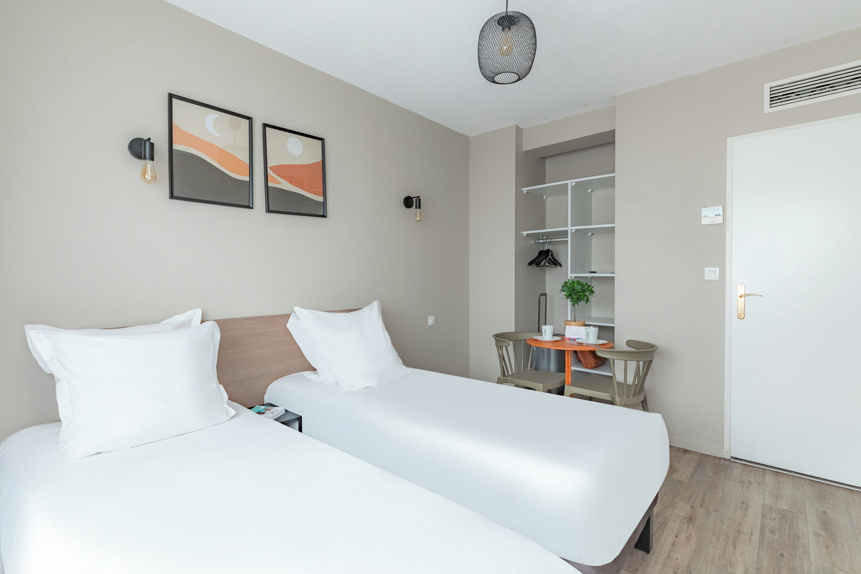 A hotel room with two beds, a small table with chairs, a potted plant, and a wardrobe.