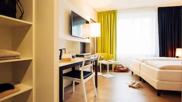 A hotel room with a bed, a desk with a chair, a television, and a window with curtains.