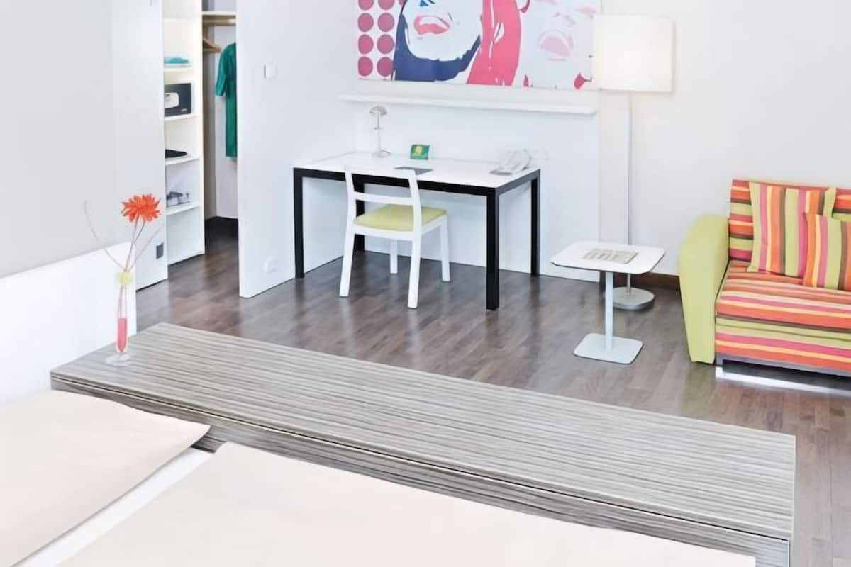 A modern room with a dining table, a chair, a small white table, a colorful sofa, and a painting on the wall.
