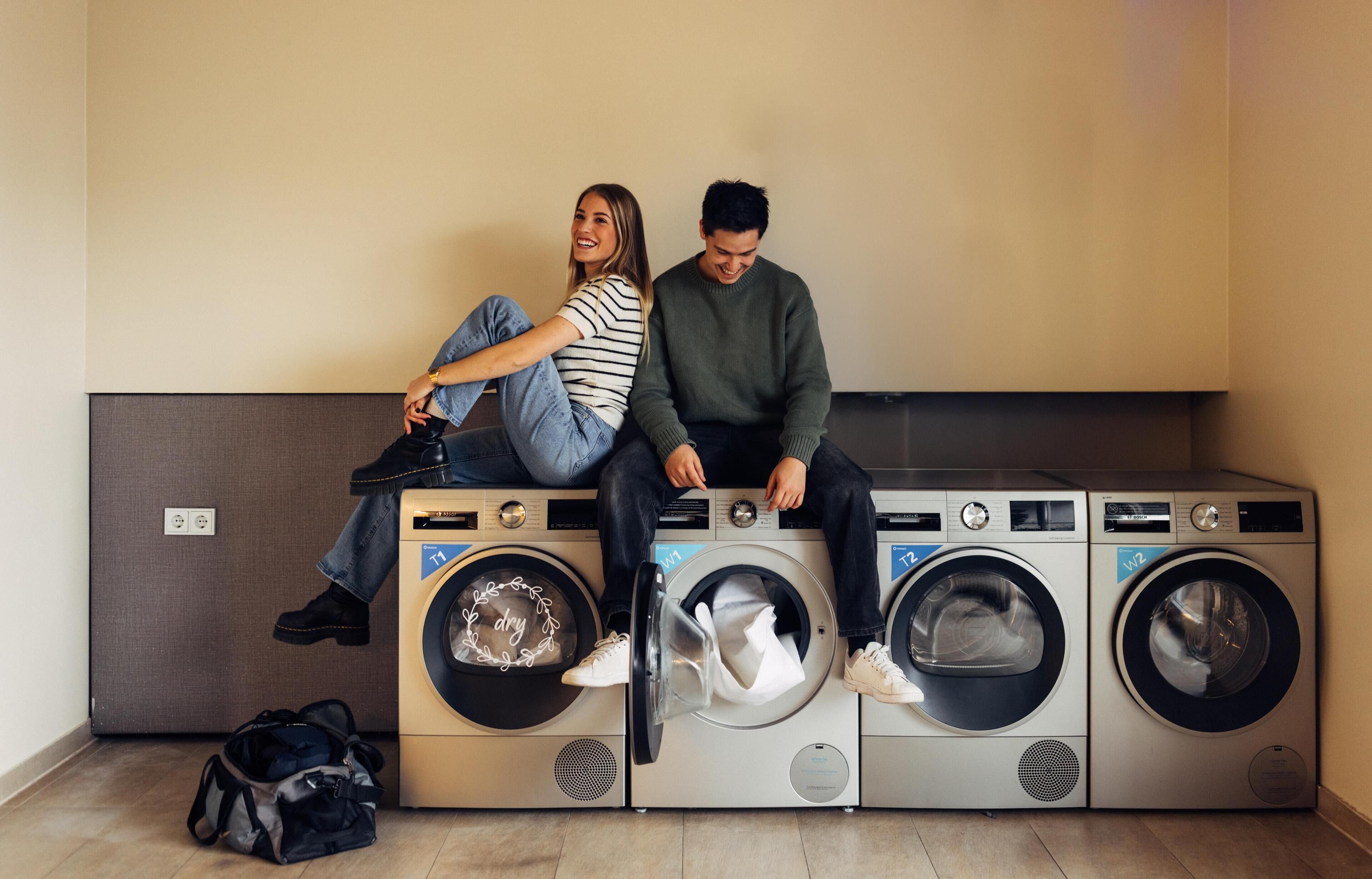 Un área de lavandería con dos personas sentadas sobre una unidad de lavadora.