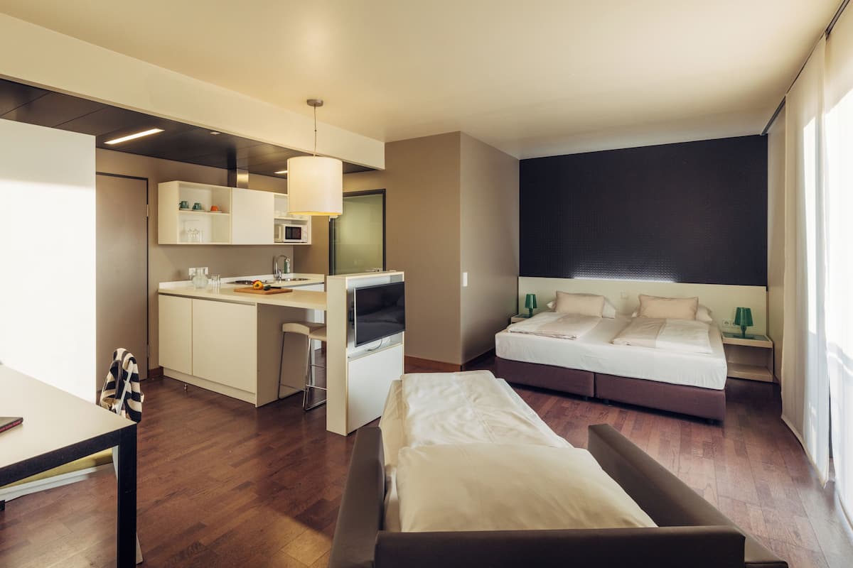 A modern hotel room with a kitchenette, a bed, and a desk.