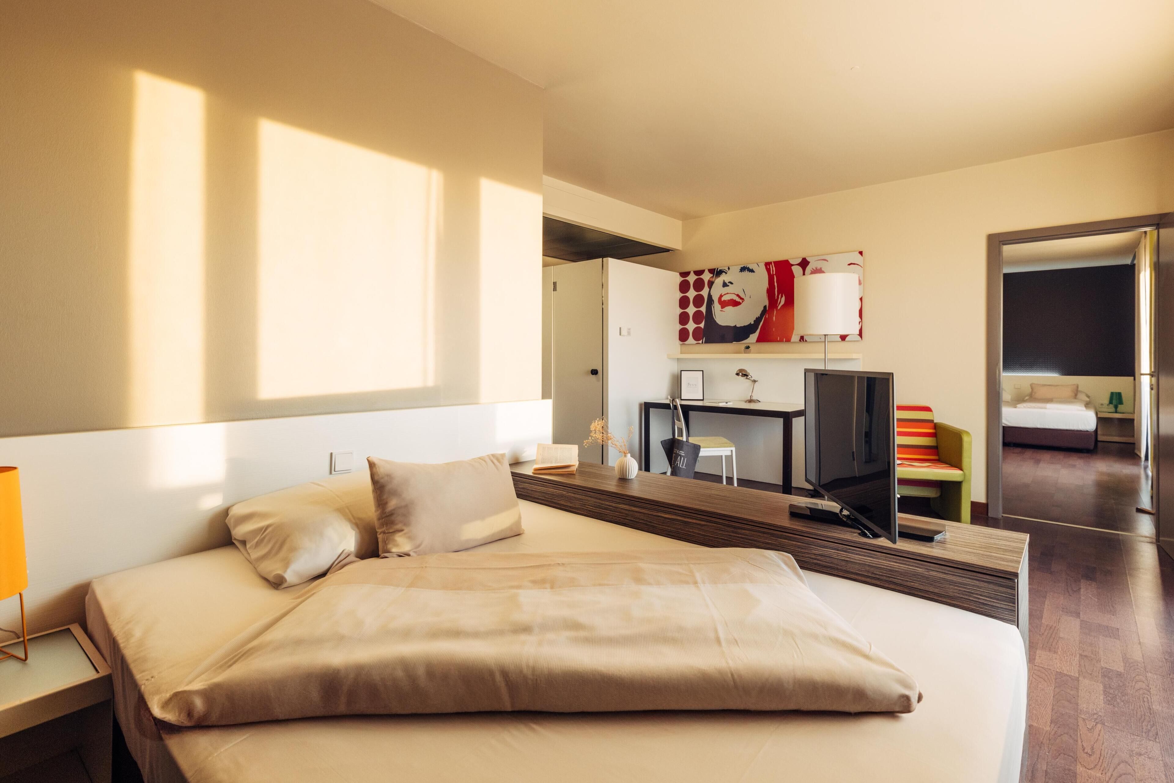 A hotel room with a large bed, a desk with a computer, a TV, and a mirror.