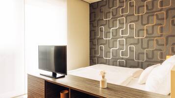 A modern hotel room with a bed, a TV on a wooden console, and a patterned wall.