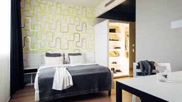 A modern hotel room with a neatly made bed, a small table, and a wardrobe with hanging clothes.