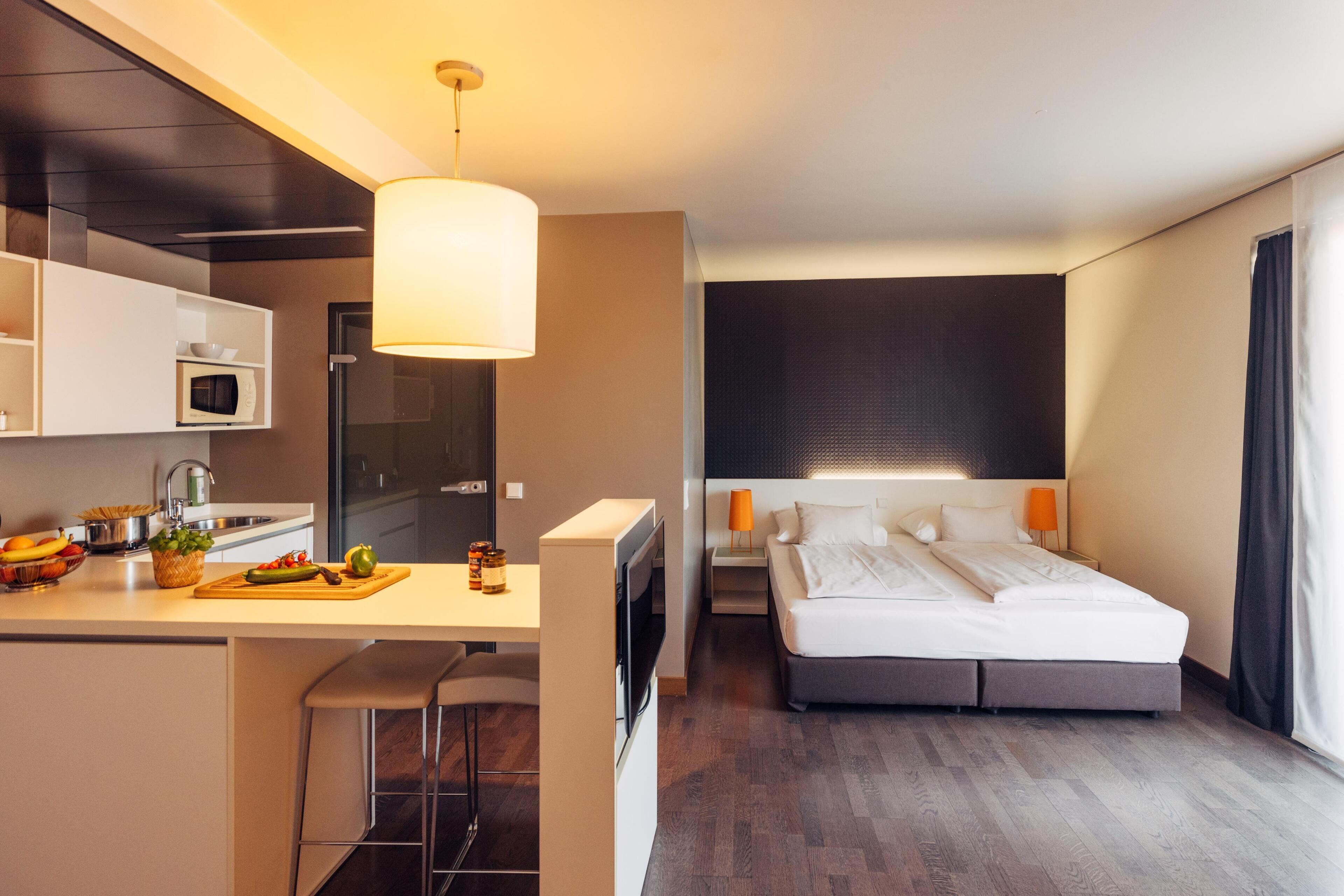 A modern hotel room with a kitchenette, a large bed, and a view of the city.