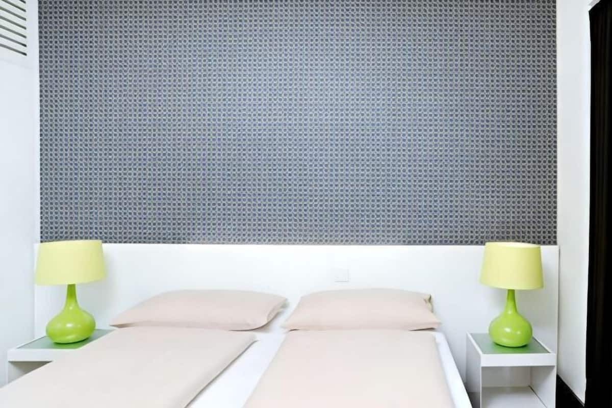 A bed with two pillows, a green lamp on each side, and a grey patterned wall behind.
