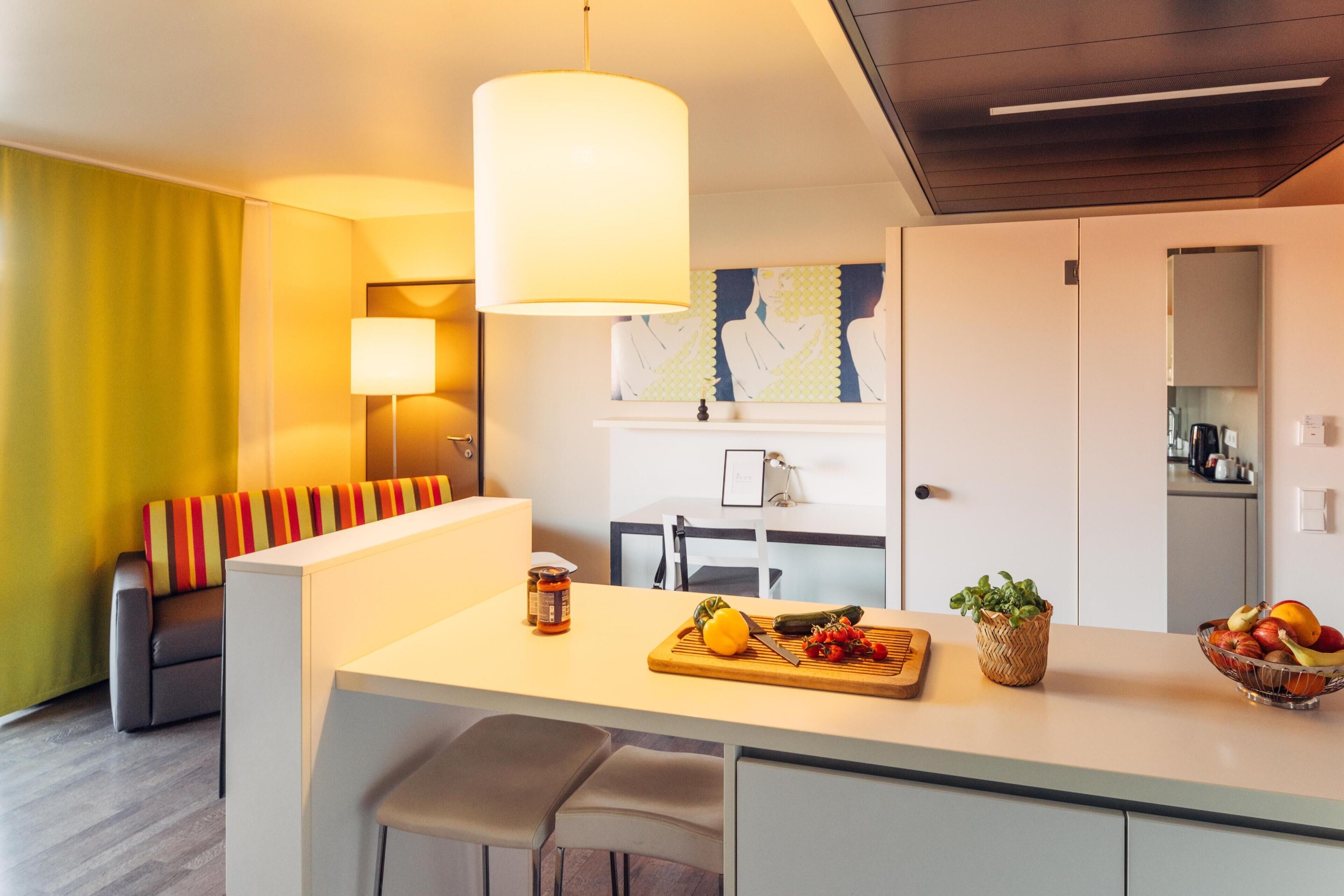 A modern kitchen with a central island, a dining area with a sofa, and a living area with a couch and a lamp.